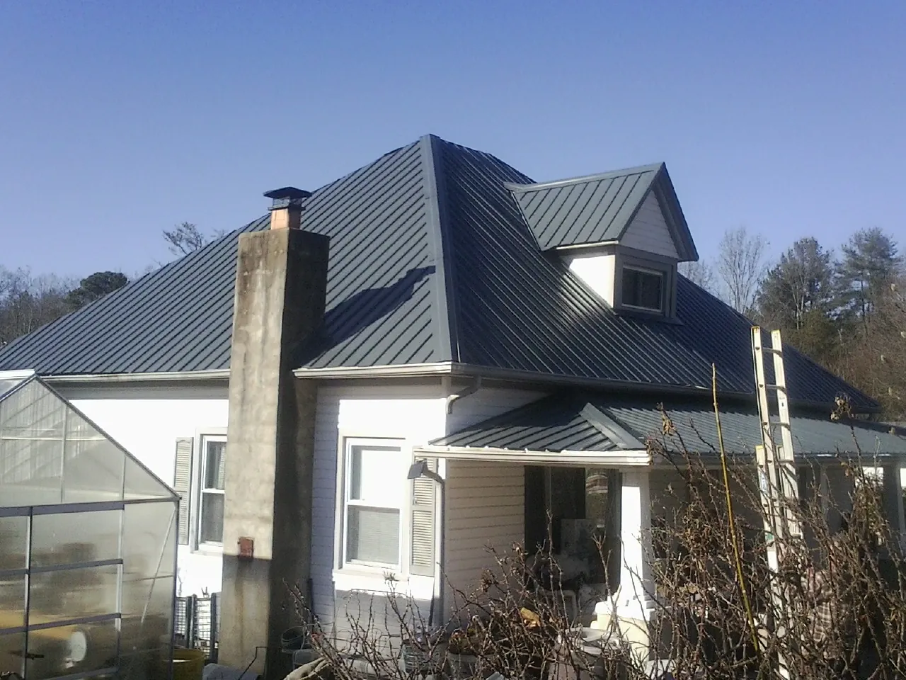 Dark blue standing seam metal roof on a white farmhouse with dormer — Slate & Tile Roof Repair by Roofing Brothers in Davey