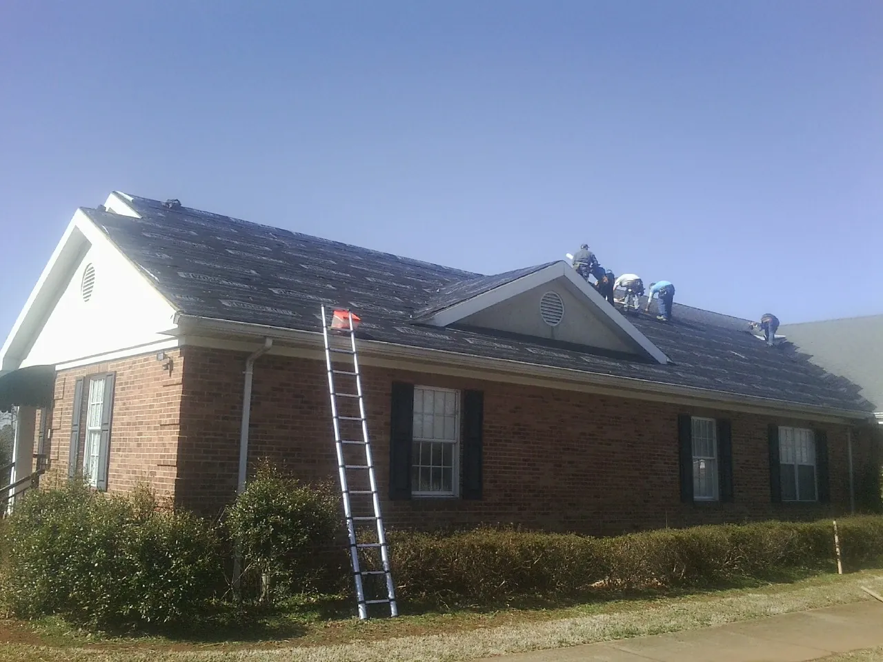 Crew tearing shingles off a brick ranch roof with a ladder set — Emergency Roof Repair work by our crew in Davey