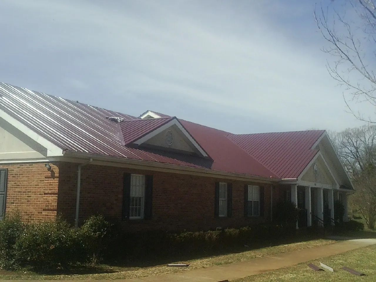 Red metal roof with gabled entries on a long brick building, from a Hail Damage Roof Repair job in Davey