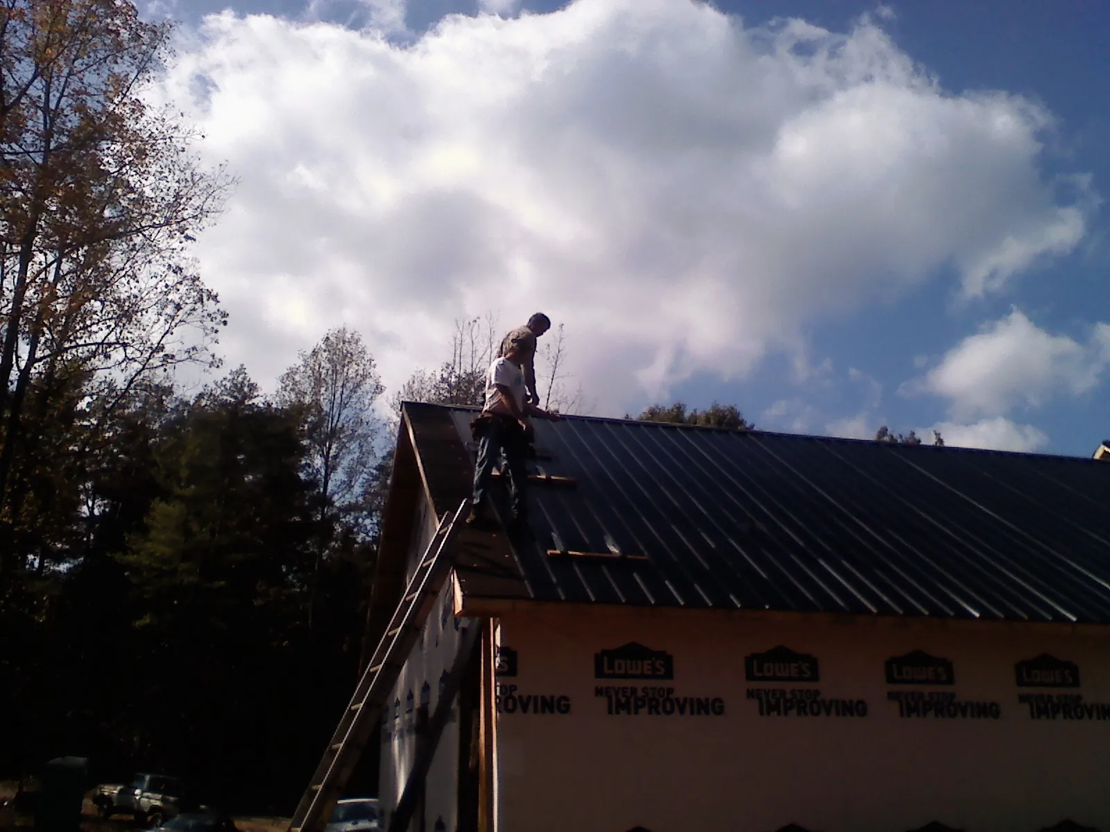 Roofer fastening dark metal panels high against a cloudy sky, from a Roof Inspection job in Davey
