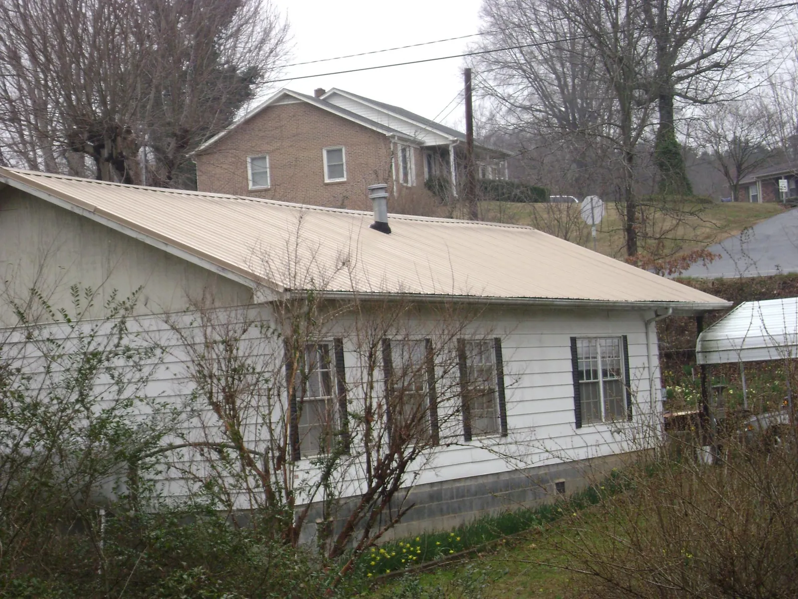 Tan metal roof on a white sided house set into a hillside — Commercial Roofing by Roofing Brothers in Davey