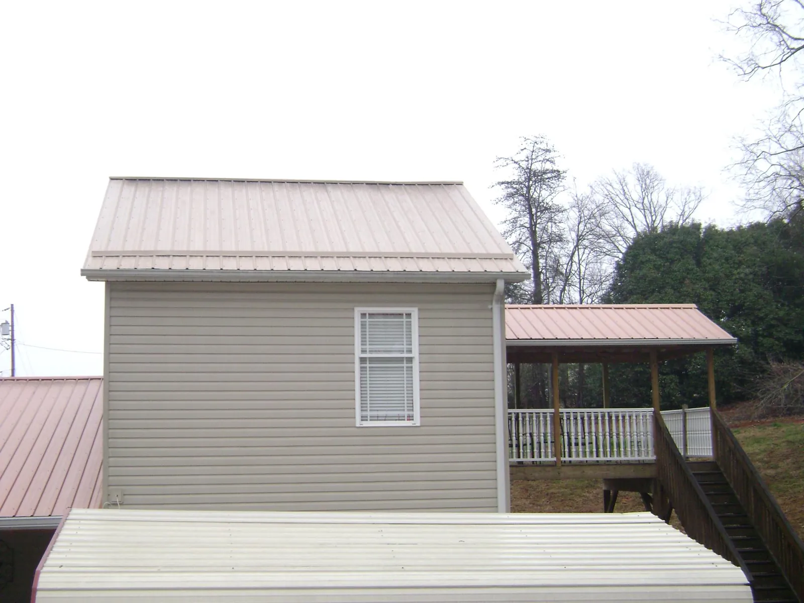 Tan metal roofs on a two story addition and attached porch, from a Roof Replacement job in Davey