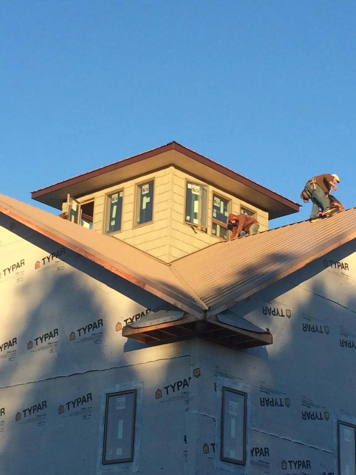 Roofers working around a rooftop cupola on a new metal roof at sunset — Roof Waterproofing in Davey by Roofing Brothers